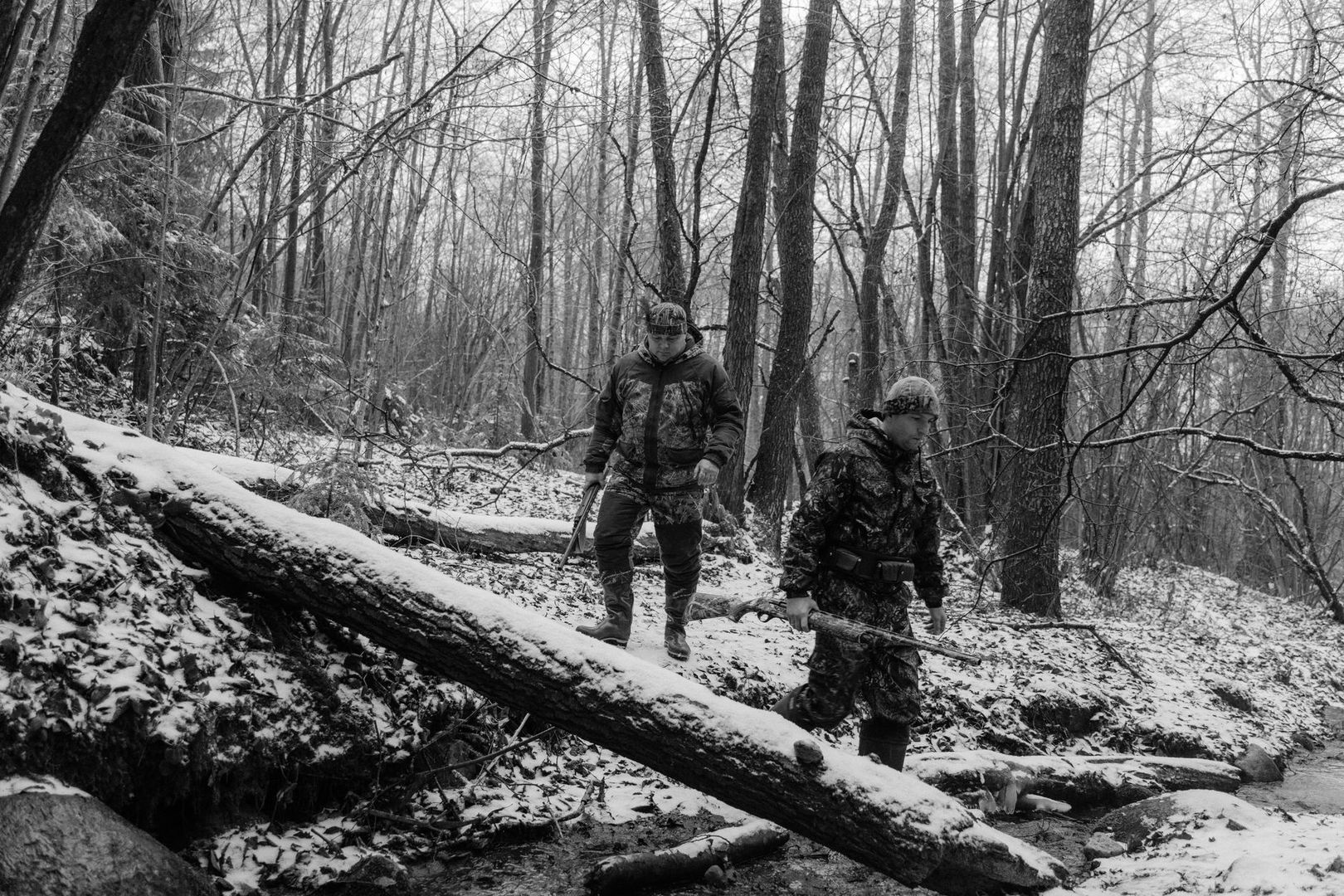Två jägare tar sig fram i snötäckt skog, var och en med gevär